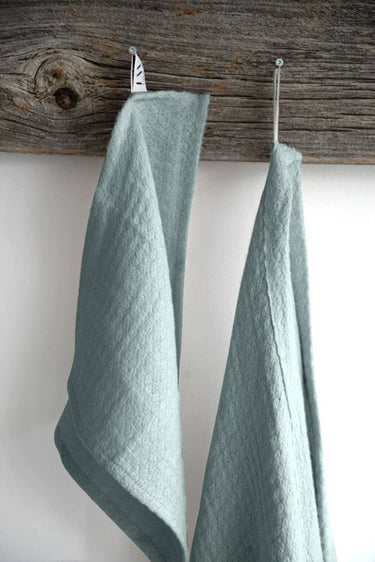 A light blue wash cloth and a matching hand towel hangs on a wooden rod against a white wall.